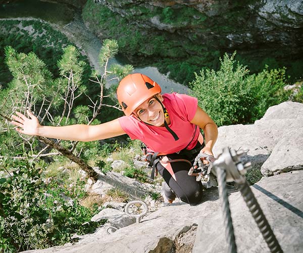 Smiling young lady climbing mountain using vera ferrata